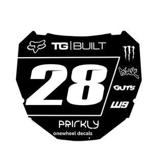 Może przedstawiać: Czarno-biała naklejka na onewheel z białym numerem 28. Naklejka zawiera logo Fox Racing, tekst "TG BUILT" i inne logo marki. Widoczny jest również tekst "PRICKLY onewheel decals".