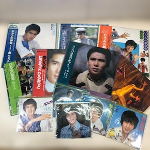 May include: A collection of vintage vinyl record albums featuring portraits of a young man. The album covers are in various colors, including white, red, green, and blue, with Japanese text and images.