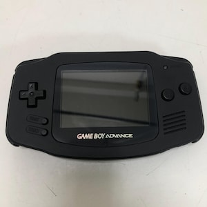 May include: Black Game Boy Advance handheld console. The device features a screen, directional pad, start and select buttons, and A and B buttons. The words "GAME BOY ADVANCE" are printed on the front of the device.