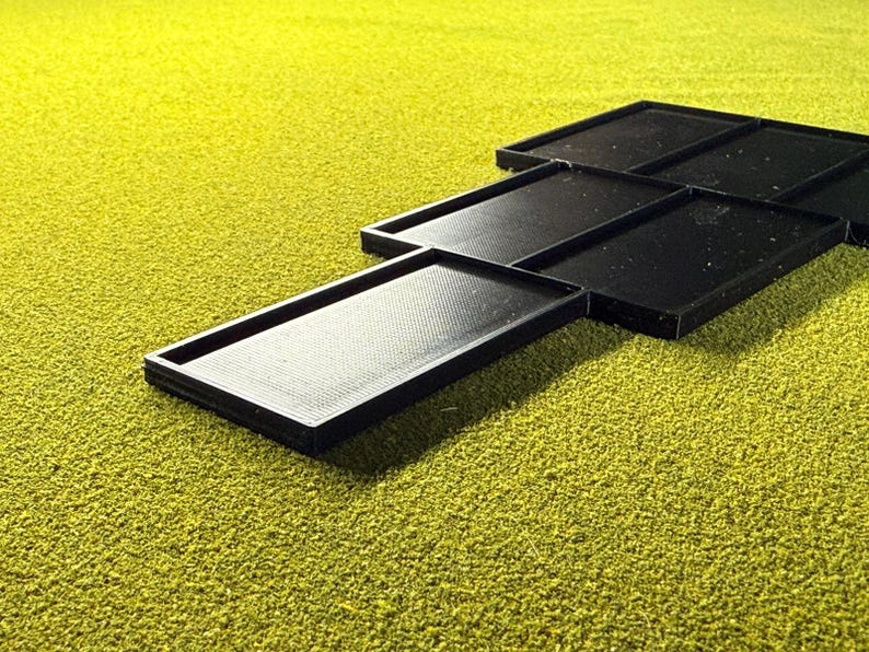 Peut inclure: Plusieurs plateaux rectangulaires noirs avec des surfaces textur&eacute;es sont dispos&eacute;s sur un fond textur&eacute; jaune-vert. Les plateaux sont faits d'un mat&eacute;riau sombre et ont un bord sur&eacute;lev&eacute;.