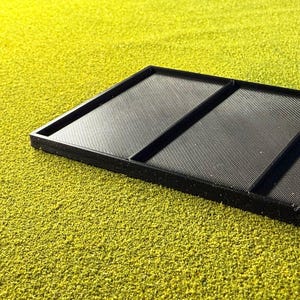 Peut inclure: Un plateau rectangulaire noir avec trois sections, chacune avec une surface textur&eacute;e et stri&eacute;e. Le plateau est pos&eacute; sur un fond jaune-vert vibrant et textur&eacute;, cr&eacute;ant un contraste de couleurs et de textures.