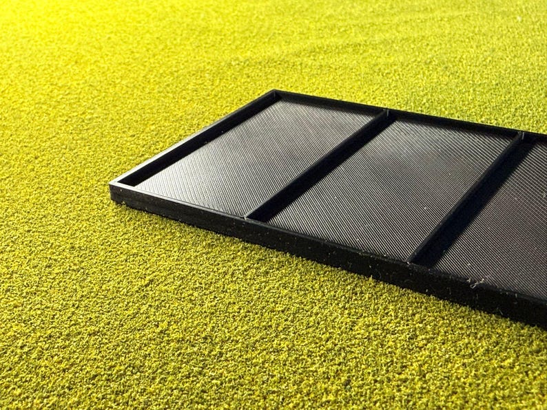 Peut inclure: Un plateau rectangulaire noir avec trois sections, chacune avec une surface textur&eacute;e et stri&eacute;e. Le plateau est pos&eacute; sur un fond jaune-vert vibrant et textur&eacute;, cr&eacute;ant un contraste de couleurs et de textures.