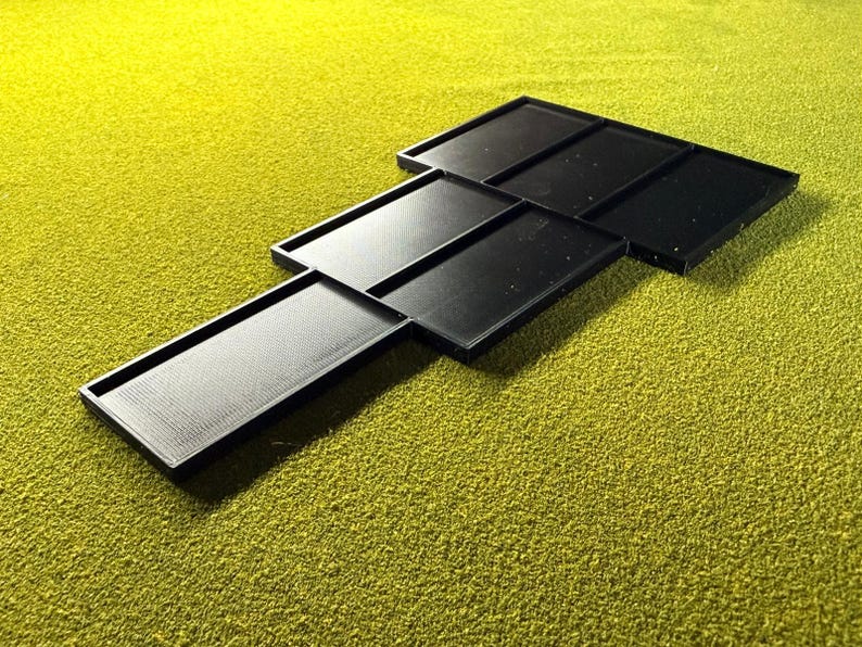 Peut inclure: Ensemble de plateaux rectangulaires noirs dispos&eacute;s en quinconce. Les plateaux ont une surface textur&eacute;e et sont pos&eacute;s sur un fond vert. Les plateaux semblent &ecirc;tre faits d'un mat&eacute;riau durable.