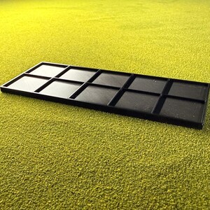 May include: A black rectangular tray with ten equally sized compartments. The tray is made of a matte black material and sits on a textured, green surface. The compartments have a textured pattern.
