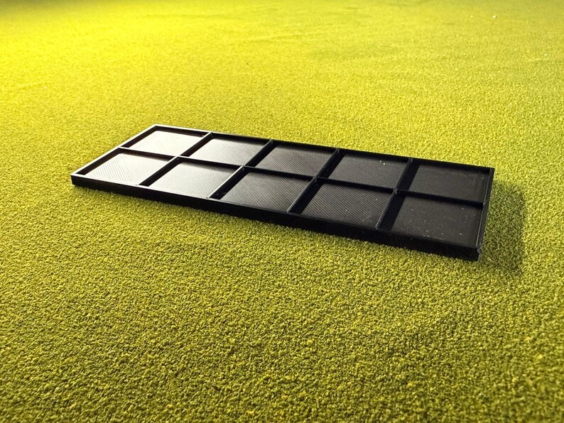 May include: A black rectangular tray with ten equally sized compartments. The tray is made of a matte black material and sits on a textured, green surface. The compartments have a textured pattern.