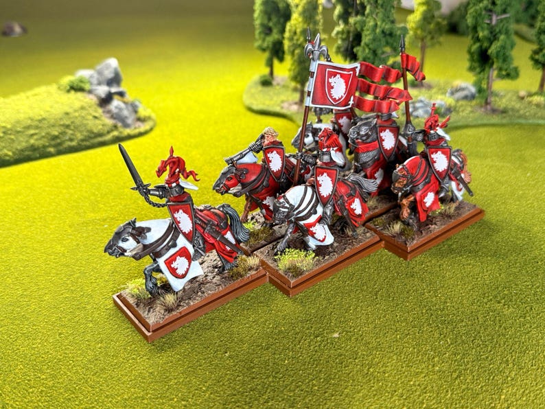 Peut inclure: Figurines miniatures de chevaliers &agrave; cheval, peintes en rouge et blanc, avec des boucliers et des banni&egrave;res. Les chevaliers sont pos&eacute;s sur une surface herbeuse verte, avec des arbres en arri&egrave;re-plan. Les figurines sont probablement pour un jeu de soci&eacute;t&eacute;.