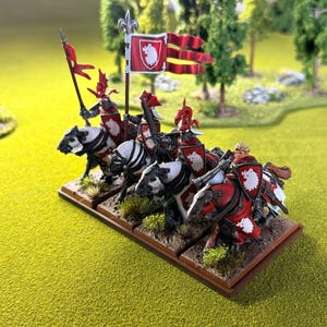 Peut inclure: Figurines miniatures de chevaliers &agrave; cheval, avec des boucliers et des banni&egrave;res rouges et blancs. Les chevaliers sont mont&eacute;s sur des chevaux noirs et blancs, et la sc&egrave;ne se d&eacute;roule sur une base verte et herbeuse. Les drapeaux portent un embl&egrave;me blanc sur fond rouge.
