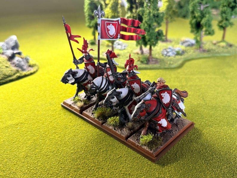 Peut inclure: Figurines miniatures de chevaliers &agrave; cheval, avec des boucliers et des banni&egrave;res rouges et blancs. Les chevaliers sont mont&eacute;s sur des chevaux noirs et blancs, et la sc&egrave;ne se d&eacute;roule sur une base verte et herbeuse. Les drapeaux portent un embl&egrave;me blanc sur fond rouge.