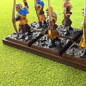 May include: Miniature archer figurines in yellow and blue, each with a bow and arrow. The figures are on individual bases, mounted on a larger brown base. The scene is set against a green, textured background.