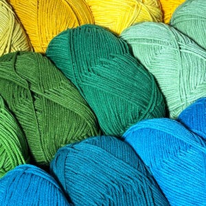 May include: A close-up shot of several skeins of yarn in various shades of green, yellow, and blue. The yarn is tightly wound, with visible strands creating a textured surface. The colors range from bright yellow to deep teal, offering a vibrant palette for crafting projects.