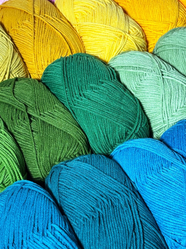May include: A close-up shot of several skeins of yarn in various shades of green, yellow, and blue. The yarn is tightly wound, with visible strands creating a textured surface. The colors range from bright yellow to deep teal, offering a vibrant palette for crafting projects.