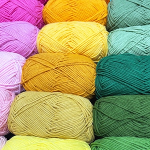 May include: A close-up shot of several skeins of yarn in various colors, including pink, orange, yellow, green, and teal. The yarn is tightly wound into neat, rounded balls, suggesting a craft or hobby project. The image is well-lit, highlighting the texture and color variations.