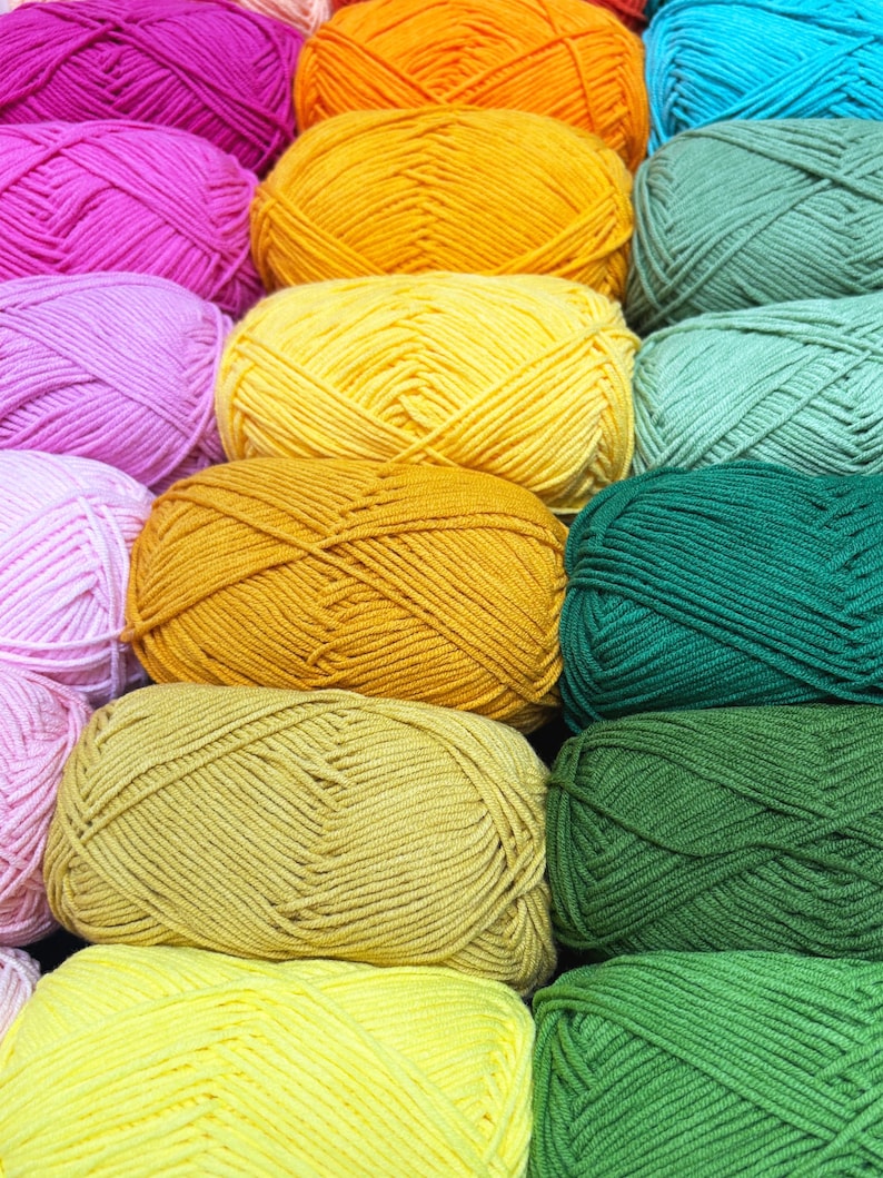 May include: A close-up shot of several skeins of yarn in various colors, including pink, orange, yellow, green, and teal. The yarn is tightly wound into neat, rounded balls, suggesting a craft or hobby project. The image is well-lit, highlighting the texture and color variations.
