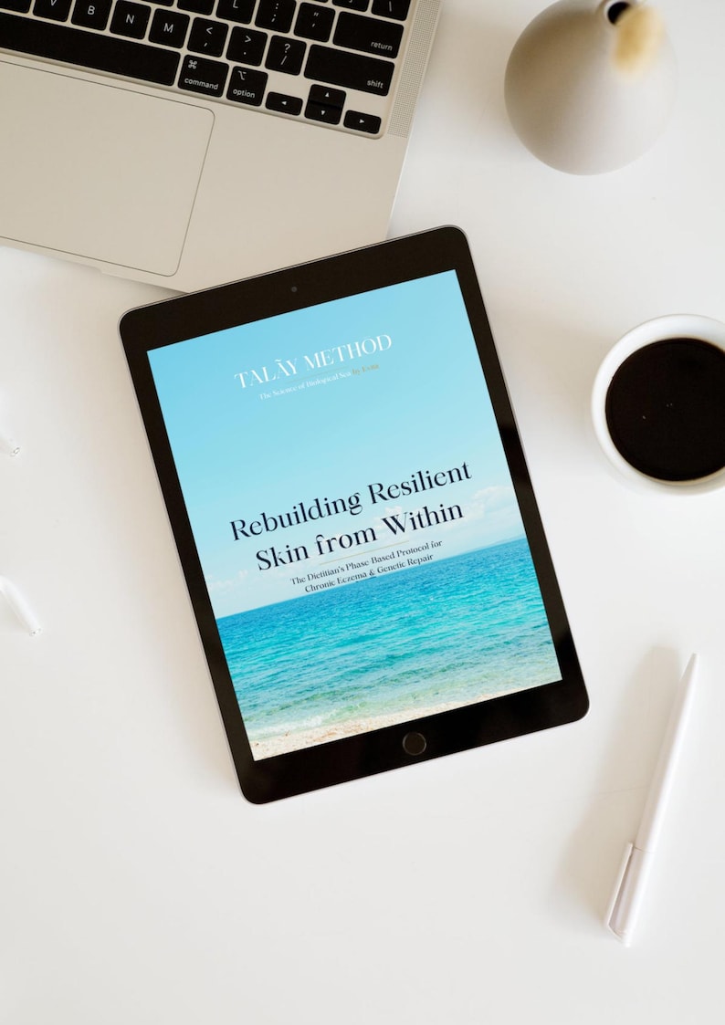 K&ouml;nnte beinhalten: Ein Tablet zeigt den Text "TALAY METHOD" und "Rebuilding Resilient Skin from Within" &uuml;ber einem blauen Ozeanbild. Ein Laptop, eine Tasse Kaffee, ein Stift und eine dekorative Vase befinden sich auf einer wei&szlig;en Oberfl&auml;che.