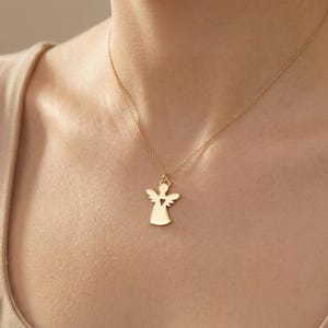 Puede incluir: Un collar con colgante de &aacute;ngel dorado. El colgante presenta una silueta de &aacute;ngel con un coraz&oacute;n recortado. El collar se lleva alrededor del cuello, con la cadena y el colgante visibles.
