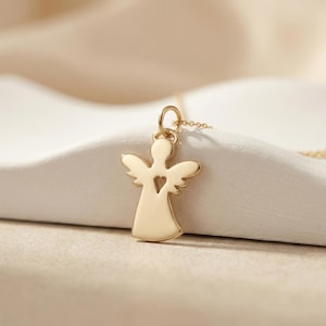 Puede incluir: Un collar con colgante de &aacute;ngel dorado. El colgante tiene forma de &aacute;ngel con un recorte en forma de coraz&oacute;n. Las alas est&aacute;n extendidas y el collar est&aacute; en una cadena dorada. El fondo es de color neutro.