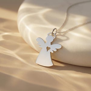 Puede incluir: Un collar con colgante de &aacute;ngel plateado. El colgante presenta una silueta de &aacute;ngel con un coraz&oacute;n recortado. La cadena del collar es delicada y plateada. El colgante mide aproximadamente 2,5 cm de altura.