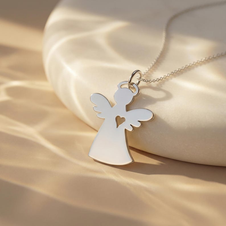 Puede incluir: Un collar con colgante de &aacute;ngel plateado. El colgante presenta una silueta de &aacute;ngel con un coraz&oacute;n recortado. La cadena del collar es delicada y plateada. El colgante mide aproximadamente 2,5 cm de altura.