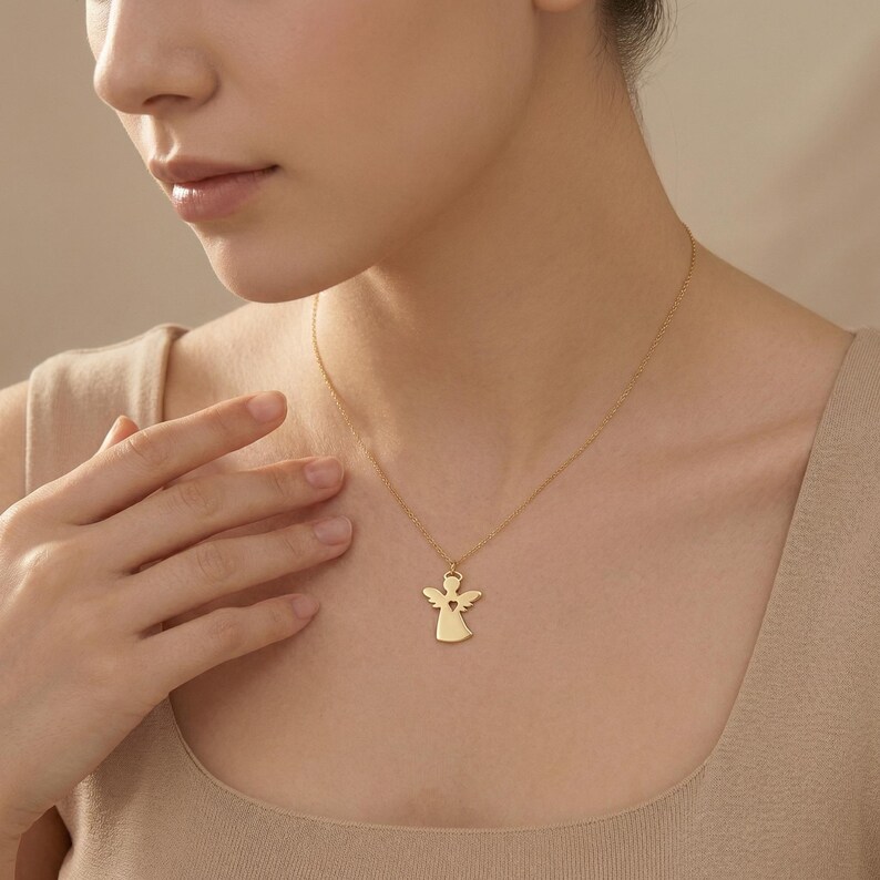 Puede incluir: Un collar con colgante de &aacute;ngel dorado. El colgante presenta una silueta de &aacute;ngel con un recorte en forma de coraz&oacute;n. El collar se lleva alrededor del cuello de una persona.