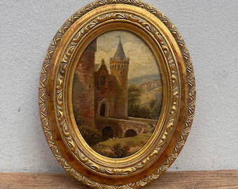 May include: An oval-shaped painting featuring a stone castle with a tall tower and a bridge, enclosed in an ornate, textured gold frame. The artwork depicts a landscape scene with muted earth tones, including brown, tan, and green hues.