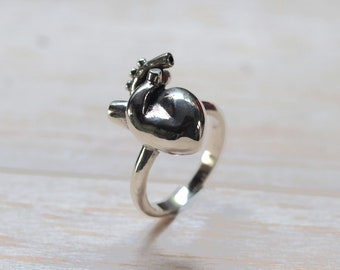 May include: A silver ring featuring a detailed anatomical heart design. The heart is three-dimensional and has a textured surface.