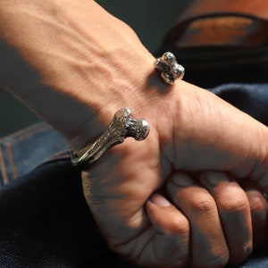 May include: A silver bracelet with a bone-shaped design. The bracelet is open and has a textured surface.