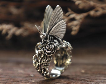 Könnte beinhalten: Ein silberner Ring mit einem detaillierten Design eines Schmetterlings, der auf einer Rose sitzt. Der Ring ist aus Metall gefertigt und hat ein zartes, filigranes Design.