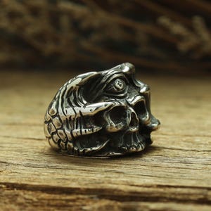 May include: A silver ring with a detailed skull design. The skull has a third eye in the center of its forehead.