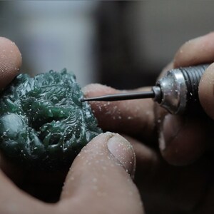 Pode incluir: Um close-up de uma m&atilde;o usando uma pequena ferramenta para esculpir uma escultura de drag&atilde;o de cera verde. A escultura &eacute; detalhada e intrincada.