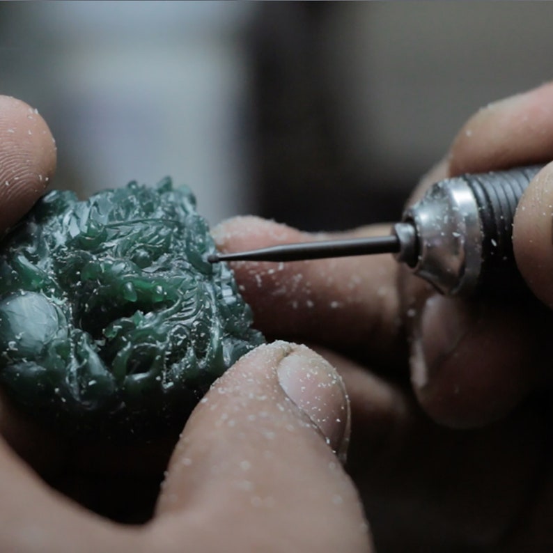 Pode incluir: Um close-up de uma m&atilde;o usando uma pequena ferramenta para esculpir uma escultura de drag&atilde;o de cera verde. A escultura &eacute; detalhada e intrincada.