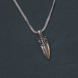 Puede incluir: Un collar de cadena de plata con un colgante de daga de plata. La daga tiene un diseño detallado y la palabra "Time" está grabada en la hoja.