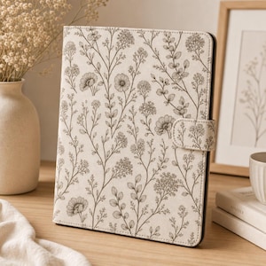 May include: A rectangular tablet case featuring a cream-coloured exterior with a repeating dark brown botanical pattern of wildflowers, stems, and leaves. The case includes a side-mounted magnetic closure tab and a black interior frame edge.