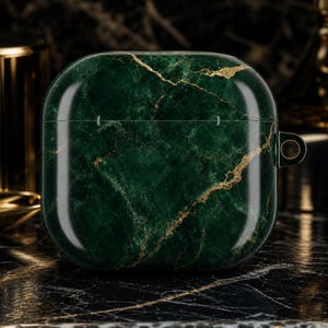 May include: A square-shaped protective case for wireless earbuds featuring a dark forest green marble pattern with intricate gold veining throughout. The case has a smooth, glossy finish and includes a small circular attachment loop on the right side.