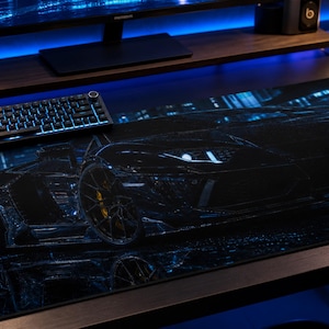 May include: A rectangular desk mat featuring a dark, high-contrast graphic of a sports car in a city at night. The design uses deep black tones with vibrant blue light accents, highlighting the car's silhouette, wheels, and reflective surfaces.