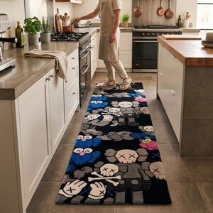 May include: A rectangular runner rug featuring a repeating pattern of cartoon-style characters with X-shaped eyes and gloved hands. The design incorporates a black background with figures in shades of blue, grey, pink, and white, laid on a kitchen floor.