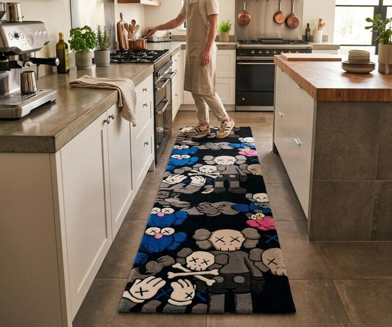 May include: A rectangular runner rug featuring a repeating pattern of cartoon-style characters with X-shaped eyes and gloved hands. The design incorporates a black background with figures in shades of blue, grey, pink, and white, laid on a kitchen floor.