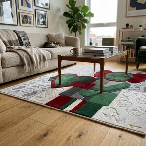 May include: A rectangular area rug featuring a large, stylised character with red and green sections, set against a light grey background with embossed skull and cross-eye motifs. The design includes geometric blocks of red, green, and white.