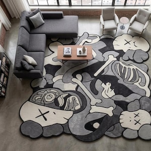May include: A large, irregularly shaped area rug featuring a monochromatic graphic design in shades of black, grey, and off-white. The pattern displays stylised skeletal elements, abstract shapes, and multiple character heads with X-shaped eyes.