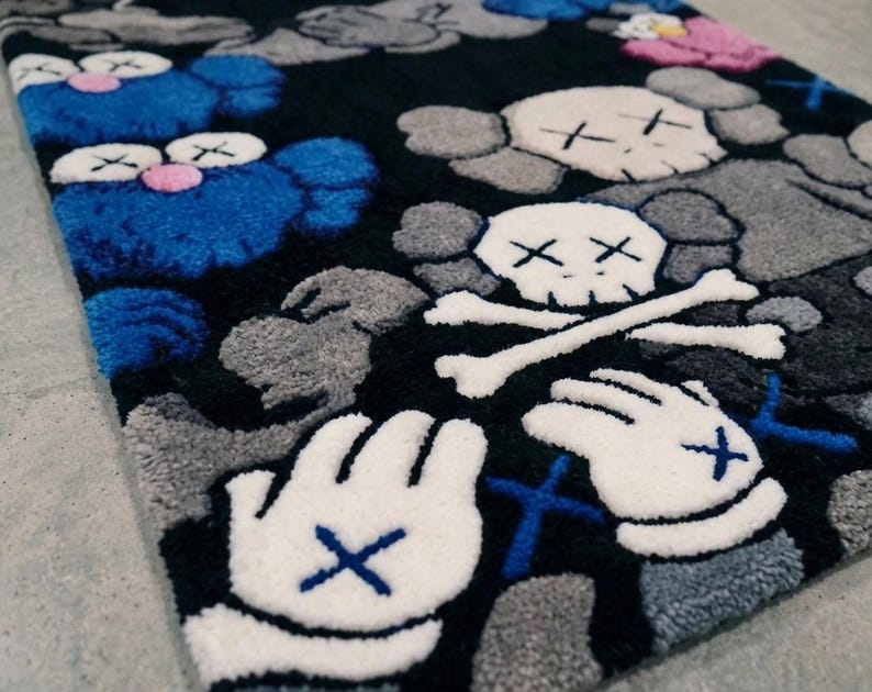May include: A rectangular tufted rug featuring a black background with a repeating pattern of blue and gray cartoon-style characters. The design includes white gloved hands with blue cross-stitch details and white skull motifs with crossbones.