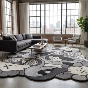 May include: A large, irregularly shaped area rug featuring a monochromatic graphic design in shades of black, grey, and white. The pattern includes stylised cartoon-like character heads with X-shaped eyes, skeletal bone motifs, and abstract shapes.
