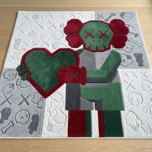 May include: A rectangular area rug featuring a central character with a green skull head, red ears, and red gloves holding a large green heart. The background is divided into white and grey sections patterned with small skulls, bones, and X-shaped eyes.