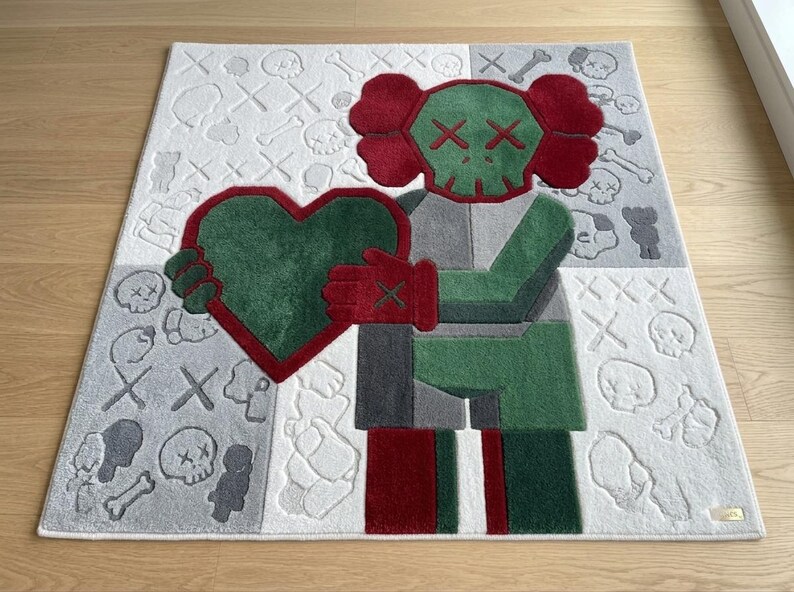 May include: A rectangular area rug featuring a central character with a green skull head, red ears, and red gloves holding a large green heart. The background is divided into white and grey sections patterned with small skulls, bones, and X-shaped eyes.