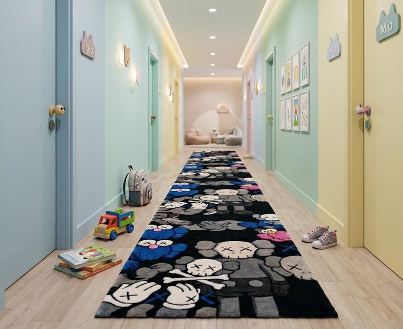 May include: A long rectangular runner rug featuring a repeating pattern of stylized cartoon characters with X-shaped eyes and skull heads in shades of black, gray, blue, and pink, laid out on a light wood floor in a hallway with colorful pastel walls.