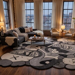 May include: A large, irregularly shaped area rug featuring a monochromatic grey, black, and white graphic design. The pattern includes stylised cartoon-like character heads with X-shaped eyes, skeletal bone motifs, and abstract organic shapes.