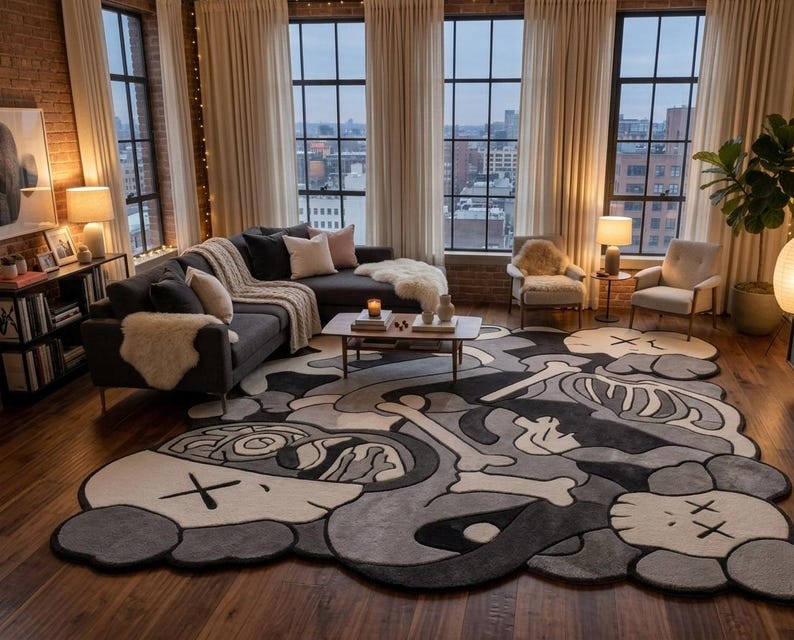 May include: A large, irregularly shaped area rug featuring a monochromatic grey, black, and white graphic design. The pattern includes stylised cartoon-like character heads with X-shaped eyes, skeletal bone motifs, and abstract organic shapes.