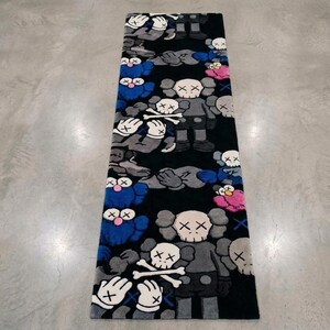 May include: A rectangular area rug featuring a black background with a repeating pattern of cartoon-style figures. The figures are depicted in shades of gray, blue, and pink, each with X-shaped eyes and white gloved hands with X markings.