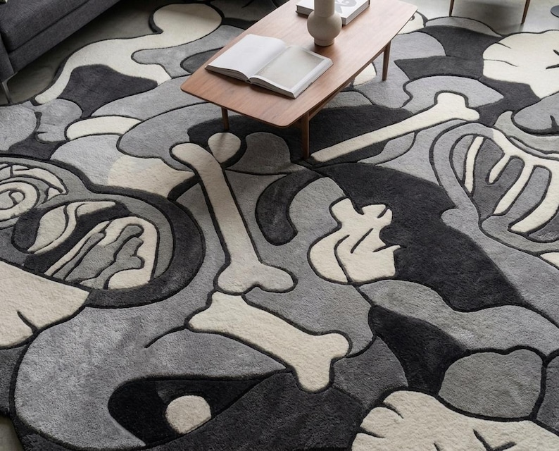 May include: A large area rug featuring a repeating abstract pattern of bones and organic shapes in shades of black, charcoal grey, light grey, and off-white. The design consists of thick, tufted lines that create a textured, layered appearance.