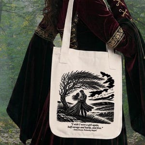 May include: A cream-colored canvas tote bag featuring a black ink illustration of a couple standing under a windswept tree. Below the image, the text reads: "I wish I were a girl again, half-savage and hardy, and free." - Emily Bront&euml;, Wuthering Heights.