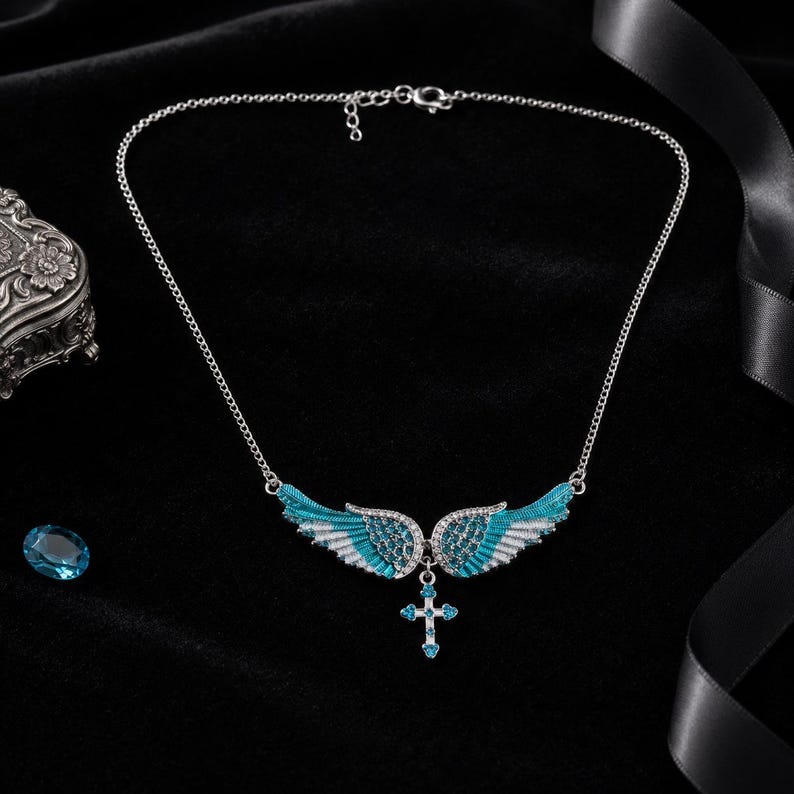 May include: A silver necklace with a pendant featuring turquoise and white wings and a cross. The wings are detailed with small, sparkling stones. The necklace is set against a black background.