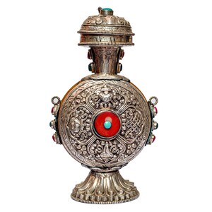 May include: A silver-toned metal vessel with a circular body, a flared base, and a removable lid. The surface features intricate embossed floral and geometric patterns, accented with a central red stone inlay and small turquoise and red cabochons.